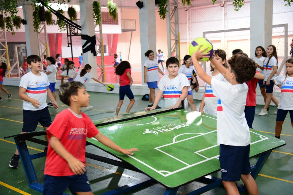 Crianças na hora do recreio brincando no pátio com mesa de futmesa.